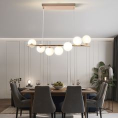 a dining room table and chairs with lights hanging from the ceiling above it in front of a white paneled wall