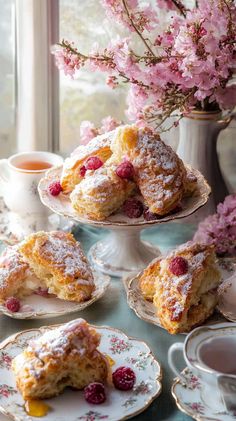 a table topped with plates and cups filled with pastries next to a vase full of pink flowers