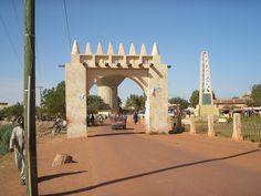 a car driving down a dirt road next to a tall arch with arches on it