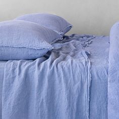 a bed with blue linens and pillows on top of it, in front of a white wall