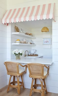 two wicker bar stools sit in front of a white counter with pink and white striped awning