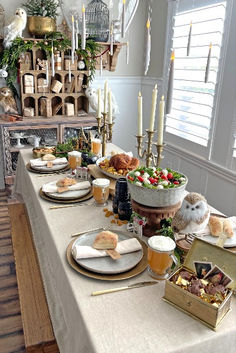 a long table with food and drinks on it in front of a shelf filled with candles