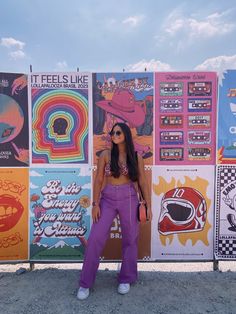 a woman standing in front of a wall with posters on it's sides and wearing purple pants