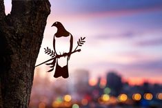 a metal bird sitting on top of a tree in front of a cityscape