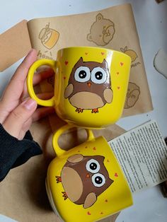 two yellow coffee mugs with an owl painted on the front and bottom one is holding a brown bear