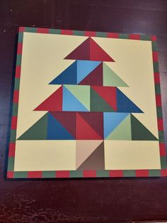 a piece of art that looks like a christmas tree on a wooden table with red, green and blue squares around it