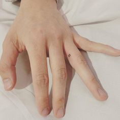 a person's left hand with a tiny heart tattoo on the middle finger, resting on a white sheet