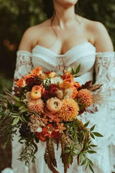 a woman in white dress holding a bouquet of flowers and greenery on her wedding day