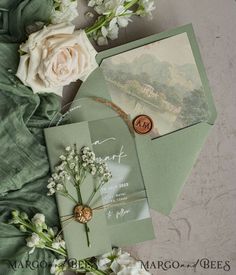 the wedding stationery is laid out on top of the green envelopes and flowers