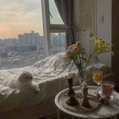 a small white dog laying on top of a bed next to a table with flowers