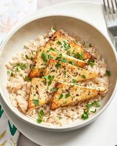 a white bowl filled with rice topped with tofu and scalloped green onions