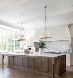 a large kitchen with an island and marble counter tops in front of two windows that look out onto the woods