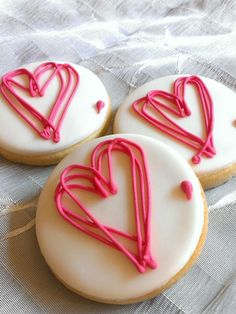 three decorated cookies with pink icing sitting on a table cloth next to each other