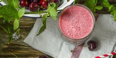 a glass filled with liquid next to some cherries on a plate and paper towel