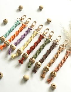 six key chains with tassels are lined up on a white surface next to beads and feathers