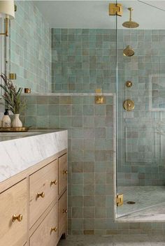 a bathroom with green tile and gold fixtures on the shower door, sink, and vanity