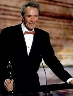 an older man in a tuxedo smiles as he stands at a podium