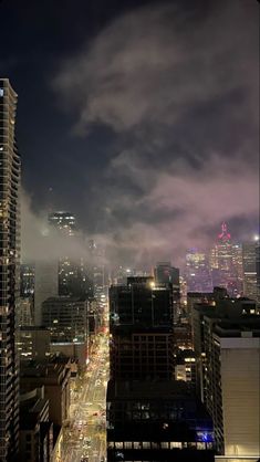 the city skyline is lit up at night with clouds in the sky and cars driving down the street