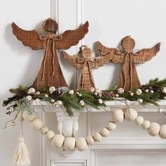 three wooden angel ornaments on top of a mantel decorated with pine cones and balls