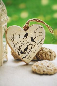 a wooden heart with two birds on it next to some sea shells and a birdcage