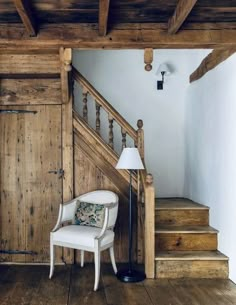 a white chair sitting next to a lamp on top of a wooden floor under a stair case