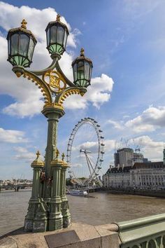 a street light sitting on the side of a river next to tall buildings and a ferris wheel