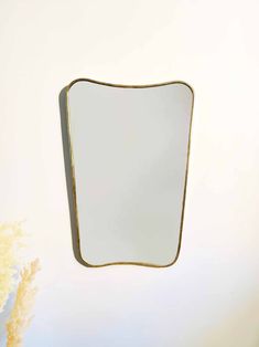 a mirror that is on the wall in front of a vase with flowers behind it