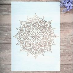 a white paper with an intricate design on it next to some purple and blue flowers