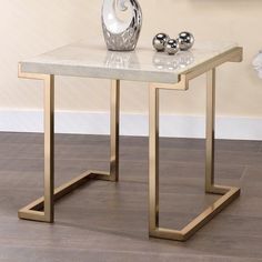 a marble table with metal legs and a vase on the top, in front of a beige wall