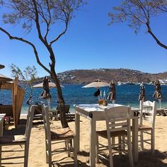 tables and chairs set up on the beach with umbrellas in the shade by the water