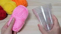 a person holding a cup with yarn in it next to several balls of yarn on a table