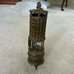 an old fashioned lantern sitting on the floor next to a white carpeted area with a chair in the background