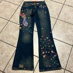 a pair of jeans with embroidered flowers on them sitting on the floor next to a tile floor