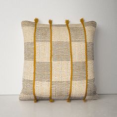 a yellow and white pillow with tassels on the sides, sitting against a wall