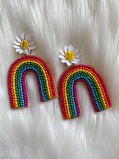 two rainbow earrings with daisies on top of white fluffy furnishing, one in the shape of a flower and the other in the shape of a letter n