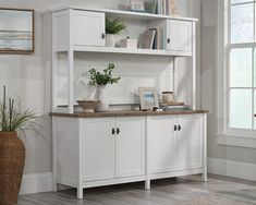 a white bookcase with plants and pictures on it next to a potted plant