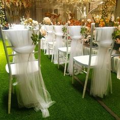 rows of white chairs with sheer sashes and flowers on them at an outdoor event