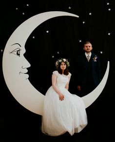 a bride and groom are sitting on the moon with stars around their heads, in front of a black background