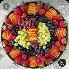 a platter filled with assorted fruit on top of a marble countertop next to sliced strawberries, grapes, and peaches