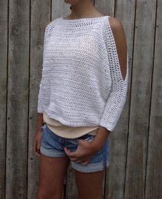 a woman standing in front of a wooden fence wearing shorts and a white knitted sweater