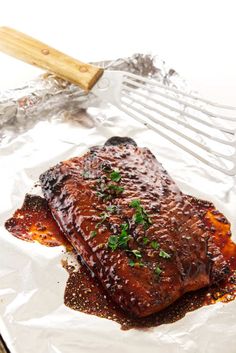 a piece of meat is sitting on foil with a spatula and fork in the background