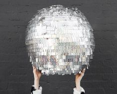 a person holding up a disco ball in front of a black wall with white fur on it