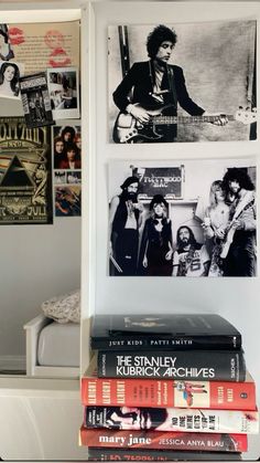 a stack of books sitting on top of a table next to a wall covered in pictures