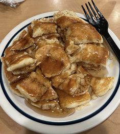 a white plate topped with pancakes covered in syrup next to a fork and knife on a wooden table