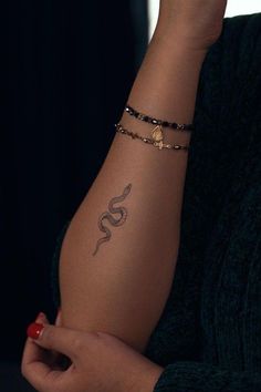 a woman's arm with a snake tattoo on her left arm and a beaded bracelet