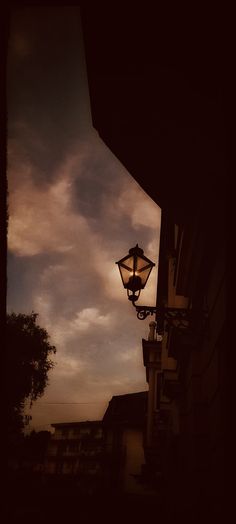 a street light hanging from the side of a building under a cloudy sky at dusk