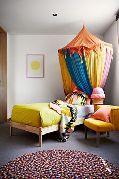 a bed room with a neatly made bed next to a yellow chair and colorful pillows