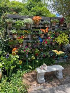 a garden filled with lots of flowers and plants next to a wooden wall covered in hanging pots