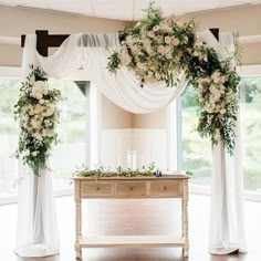 a table with white flowers and greenery on it in front of an open window