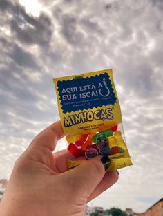 someone holding up a bag of gummy bears in front of the sky with clouds